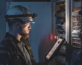 Elektryk w kasku z latarką sprawdza na tablecie schemat instalacji elektrycznej, wykonując pomiary natężenia oświetlenia awaryjnego.