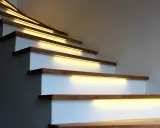 Nowoczesne lampy na klatkę schodową subtelnie oświetlają drewniane stopnie, tworząc ciepłą i bezpieczną atmosferę.